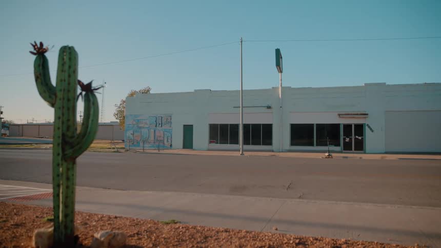White pickup truck driving past a commercial building with a cactus in the foreground