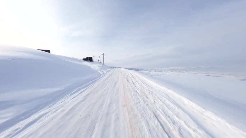 Utility poles and small buildings stand alongside a snow covered mountain road