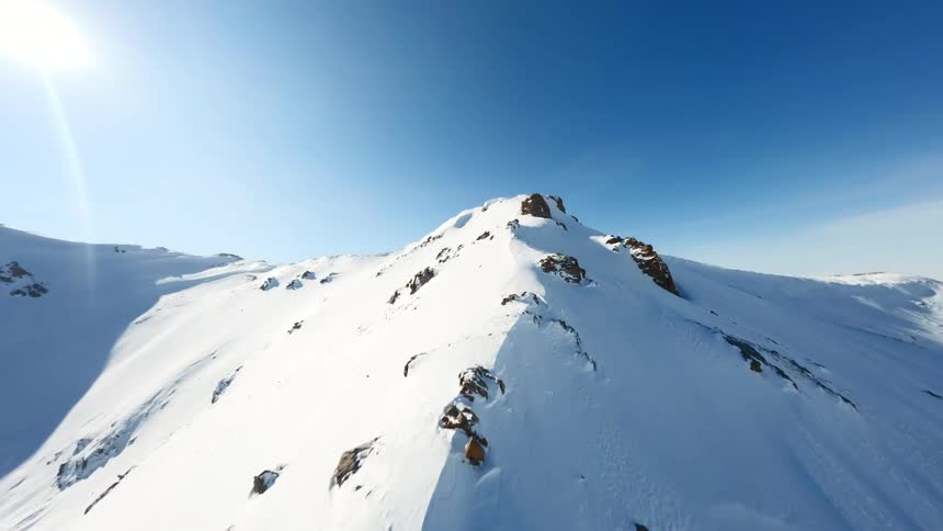 Rocks on a snow covered mountain ridge as the sun shines brightly in the sky