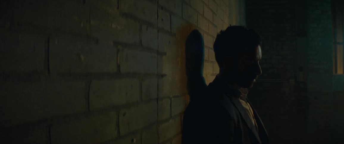 Man leaning against a brick wall in dark room