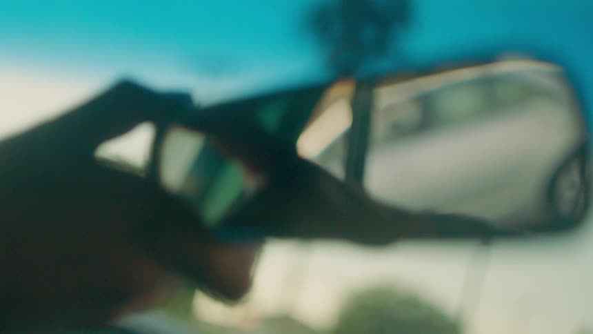 A hand adjusts a car's rear view mirror
