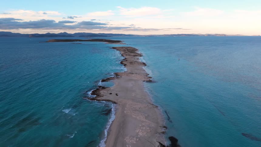An aerial view of platja de ses illetes on the island of formentera at midday with gentle ocean waves washing onto the shoreline
