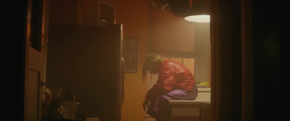 Woman sitting and dancing on kitchen counter while light flickers above her