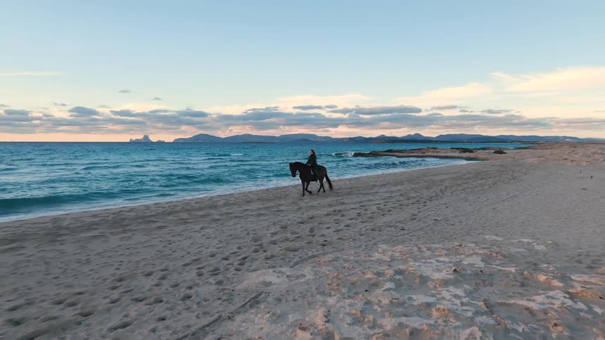 Woman rides her horse across the beach as waves roll in to shore