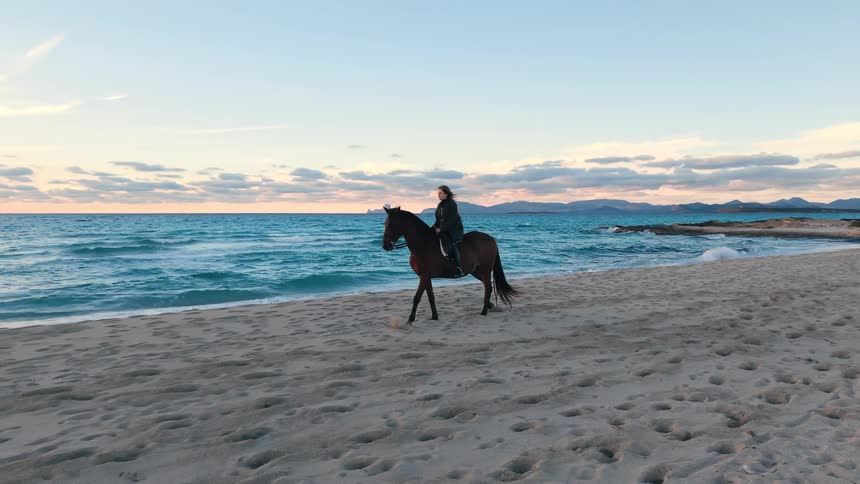 Person riding a horse on the sand by the sea with waves and mountains in the background