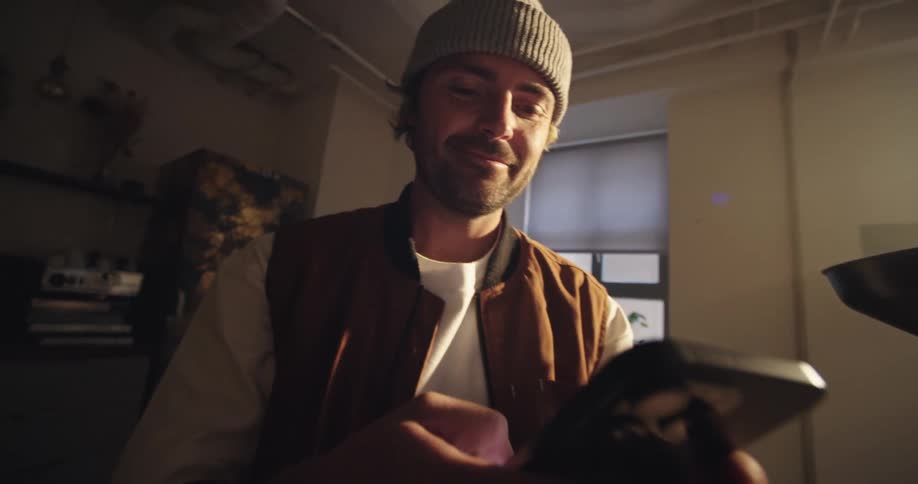 Skater looking man chilling in a room, picking up his smartphone and smiling