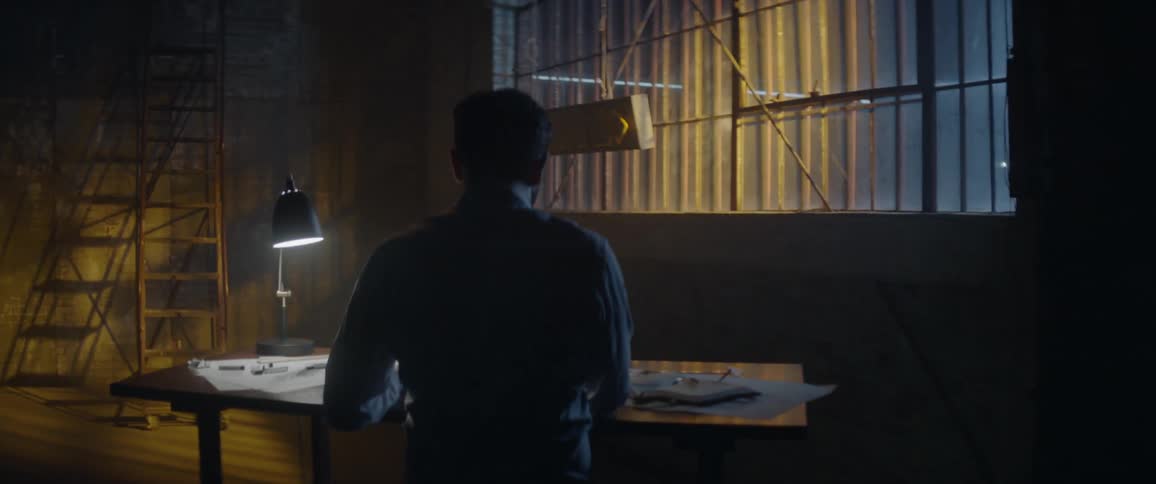Man sits at desk in a dimly lit workshop