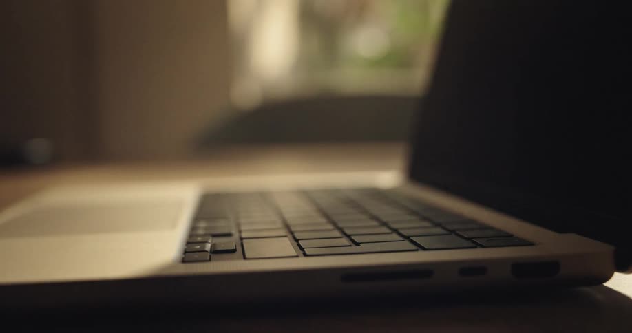 close up of a hand opening a laptop and pressing a button in indoor setting with soft lighting