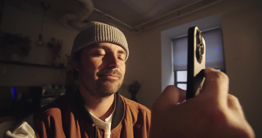 Man wearing beanie holding smartphone indoors with warm lighting