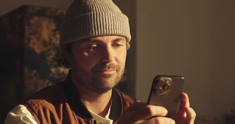 Close up of man in a beanie using his smartphone indoors