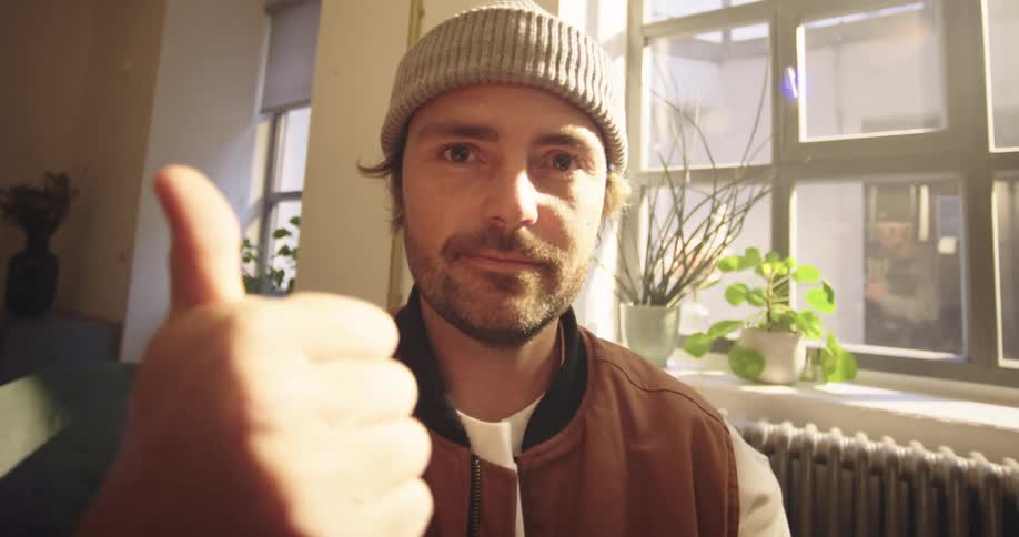 A man with tattoos types on a laptop and then looks at the camera to give a thumbs up