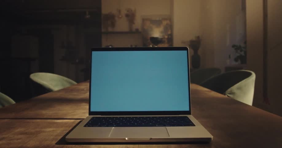 Hand closing laptop on wooden table in indoor setting with low lighting