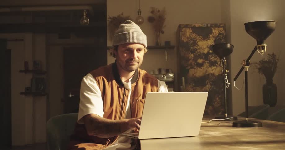 Slow zoom of a man sitting in a co working space, as he types on his laptop and then closes it