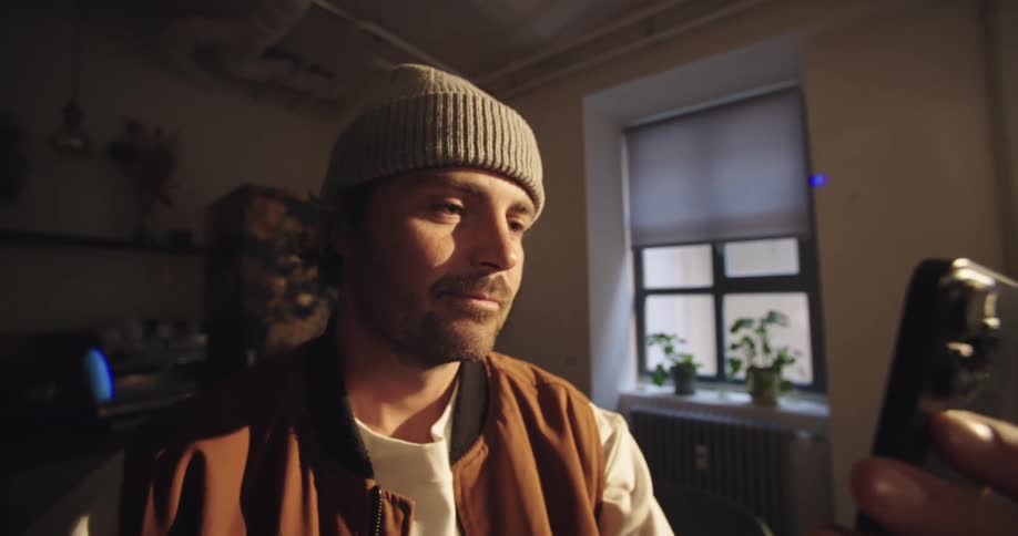 Man sitting in a room as he looks at the screen of his phone
