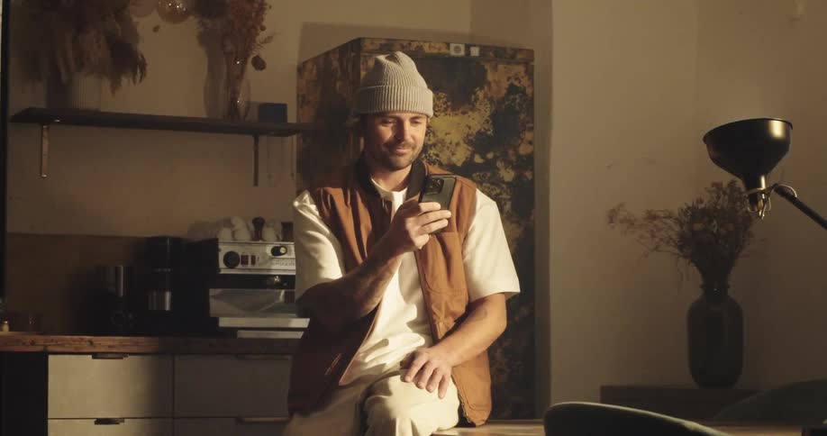 stylish man lost in thoughts, smiles at his smartphone while the camera zooms in on him