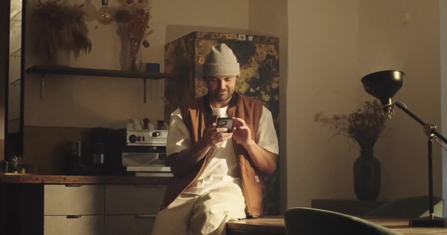 Man sitting in an open office, looking at his smartphone and smiling, receiving a funny message