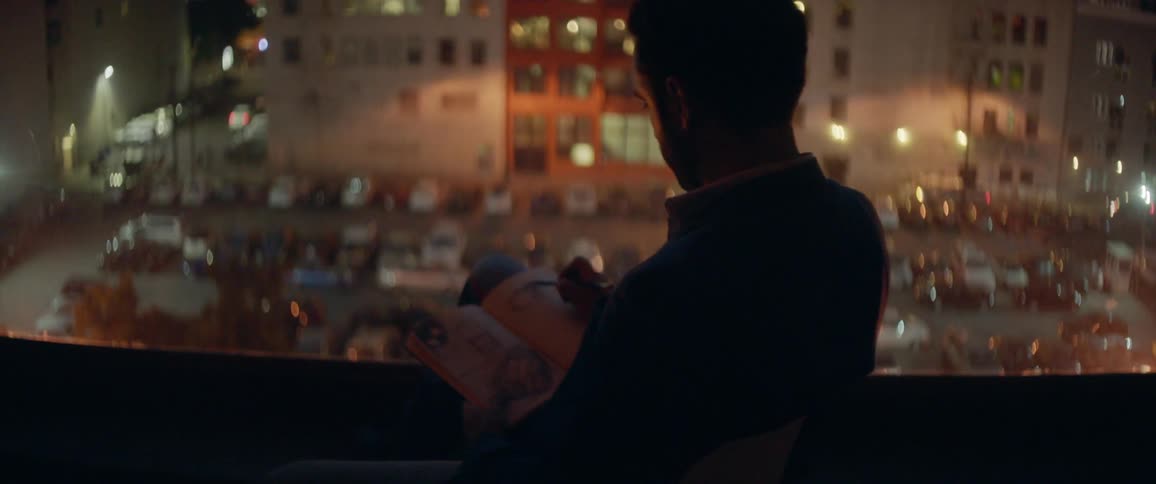 A man sits on a balcony sketching in a notepad