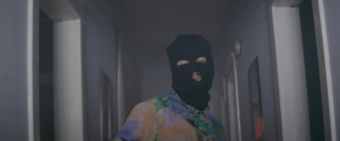 A person in a ski mask dances in a hallway with lights flashing