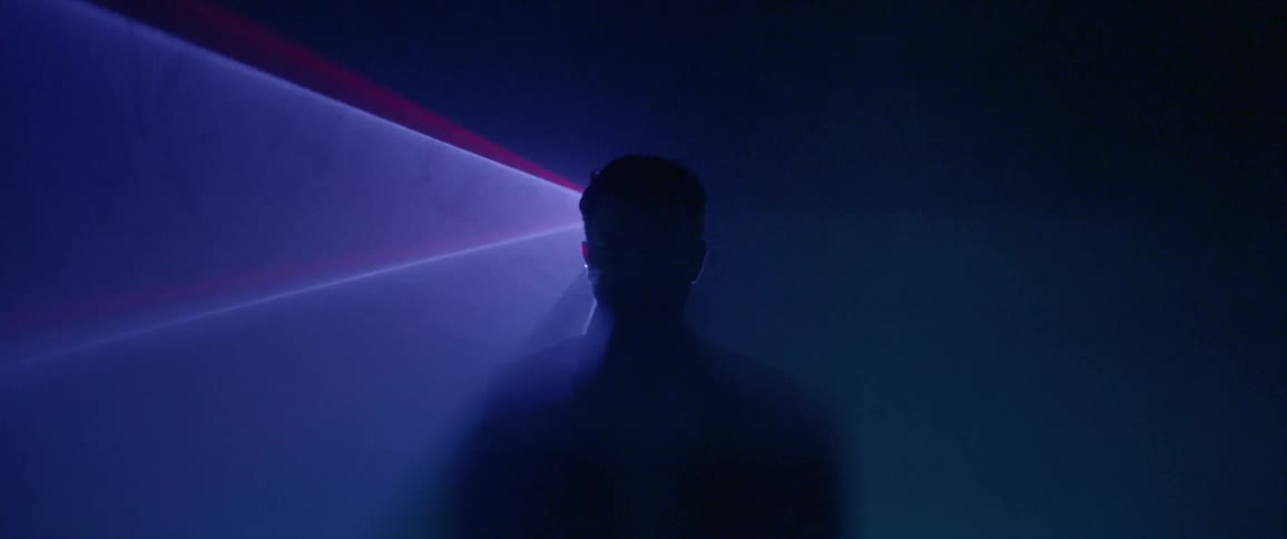 Man standing still in dark room with flashing lights behind him