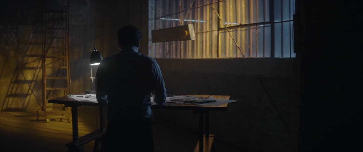 A man works at a drafting table with a lamp
