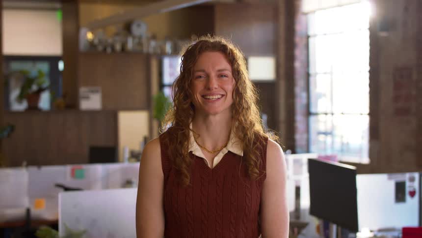 Woman smiling in office with desks computers and windows in the background