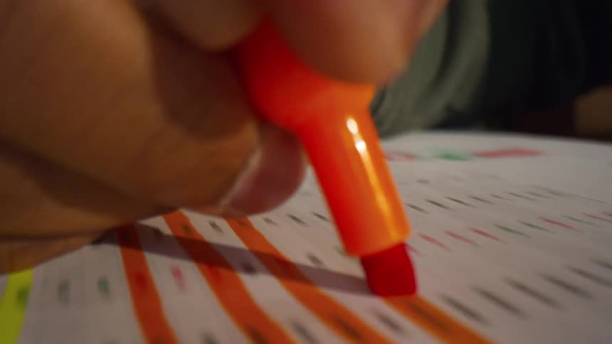 Orange highlighter marking lines of text on sheet of paper on wooden table