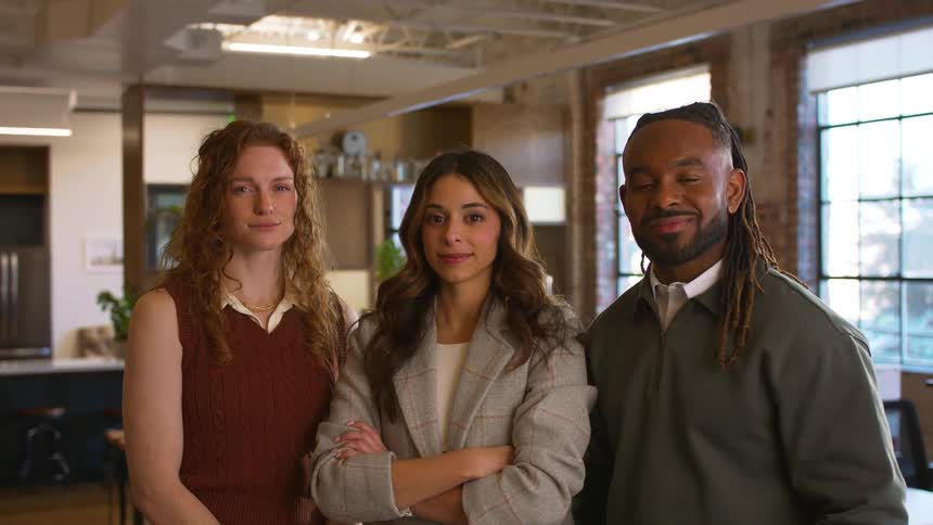 Three professionals posing together in office with desks and windows in the background