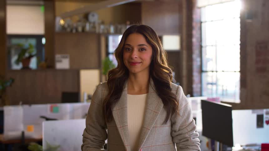 Woman in office wearing gray blazer in front of desks and computers