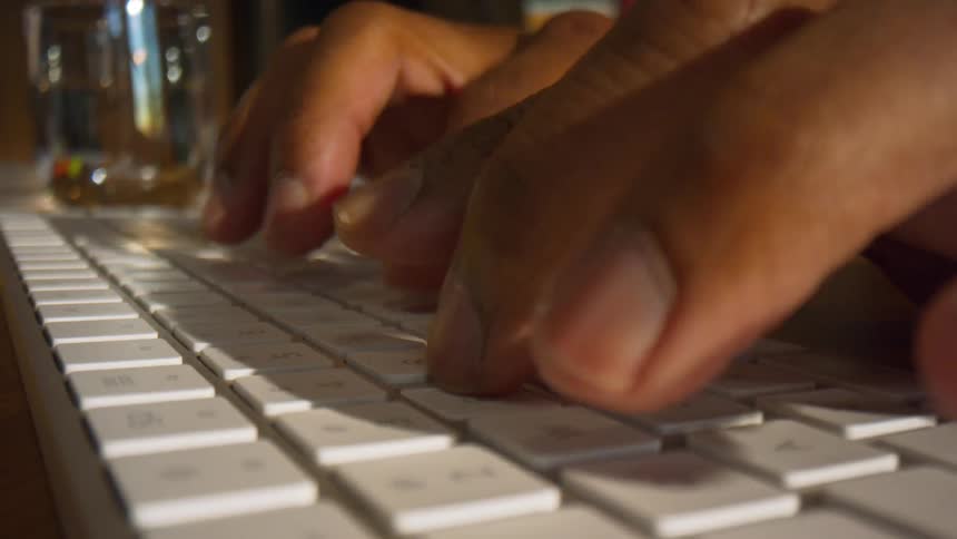 A persons hands typing on a white slim keyboard on a wooden desk
