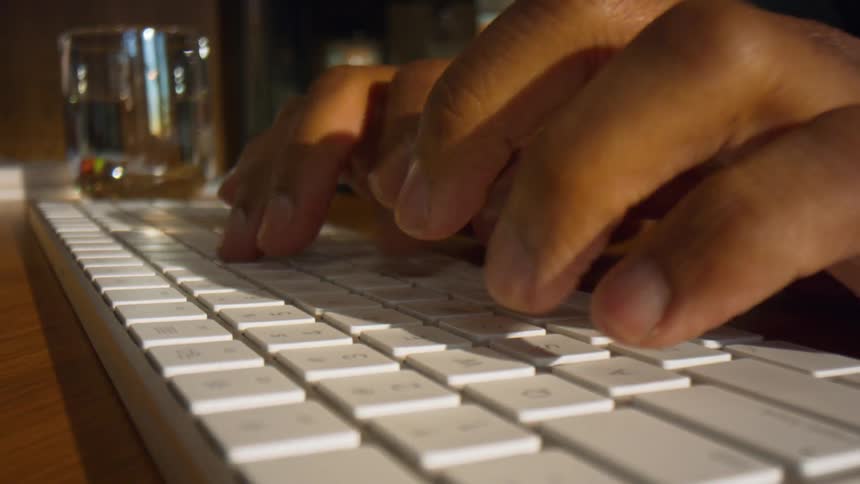 Hands typing on white keyboard with glass cup in the background on table