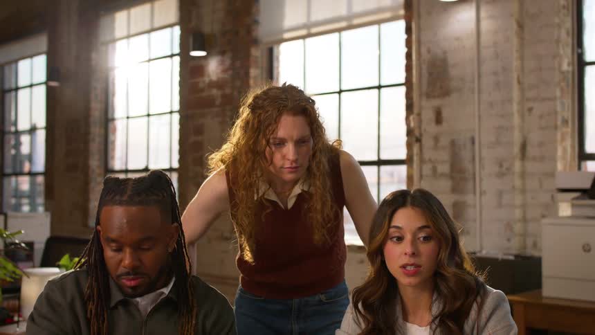 Three coworkers sit together as one discusses information displayed on a laptop
