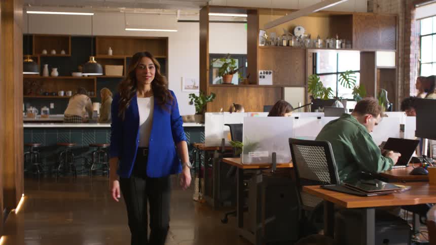 Woman walks through a shared office with colleagues working at desks and computers