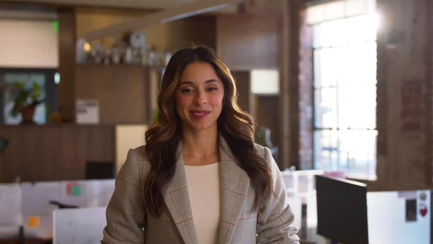 Woman smiles in an office with desks computers and windows in the background