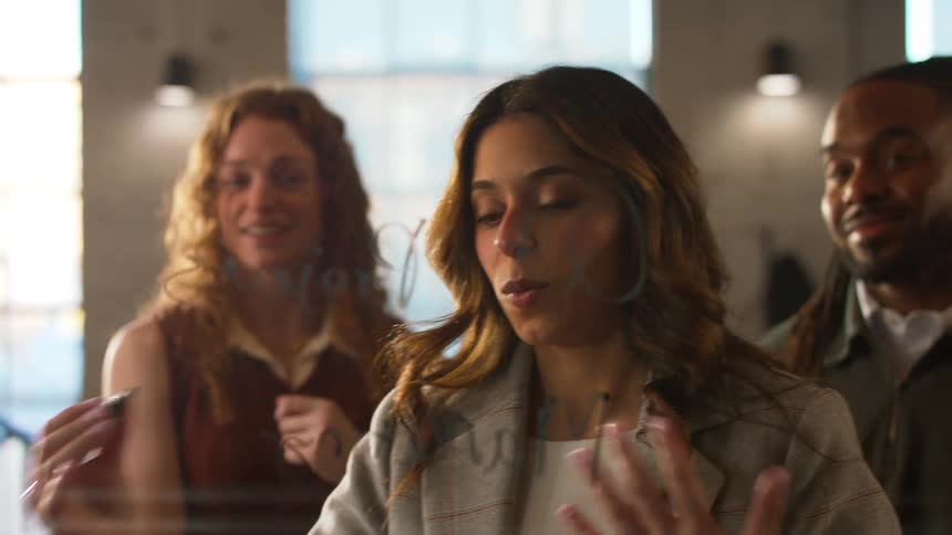 Woman writes on a glass surface while two colleagues watch in the background