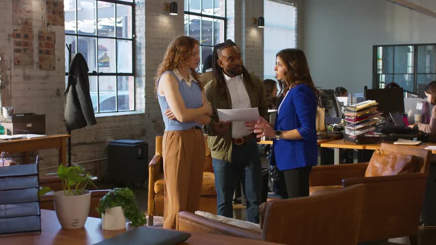 Group of coworkers reviewing document in open office with desks and large windows