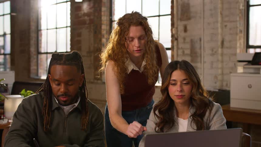 Three diverse colleagues collaborate on a laptop and documents in a modern office