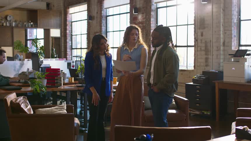Team talking in open office with desks chairs and large windows in the background