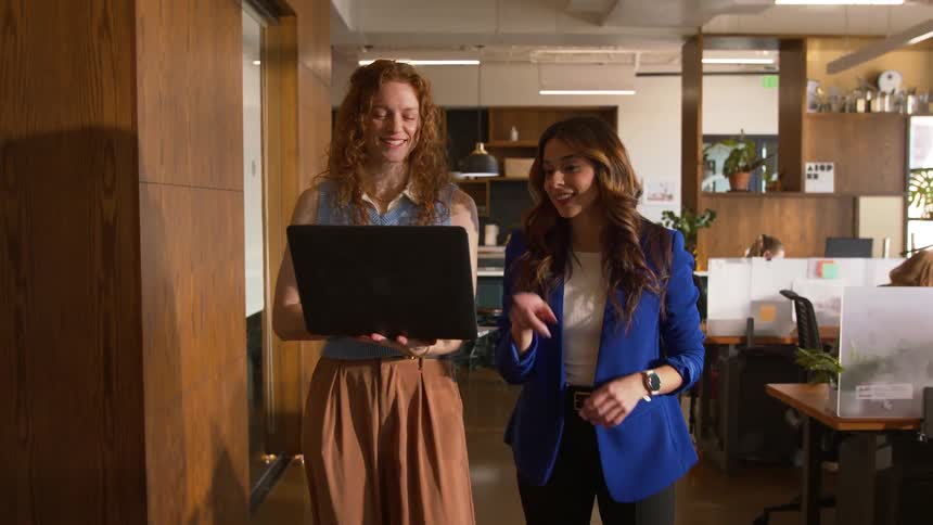 Two women are walking through the office and talking