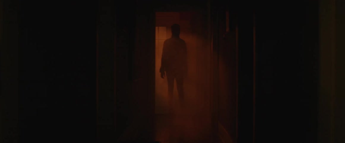 A man walks down a smoky hallway with flashing lights