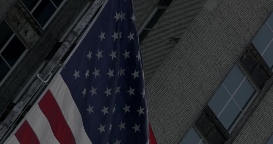 American flag flapping in the wind near a city building