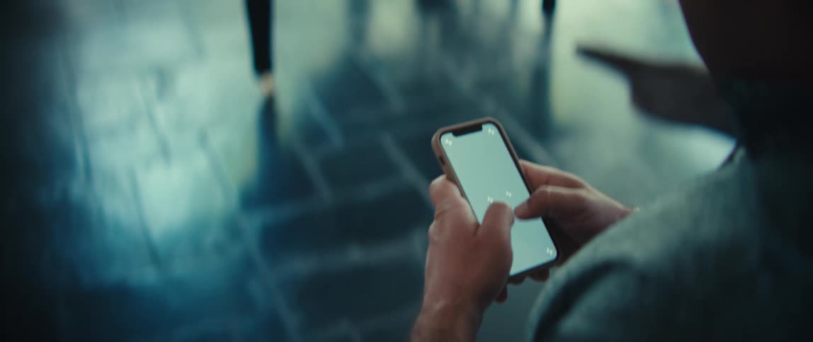 Person holding smartphone with both hands indoors with dark floor
