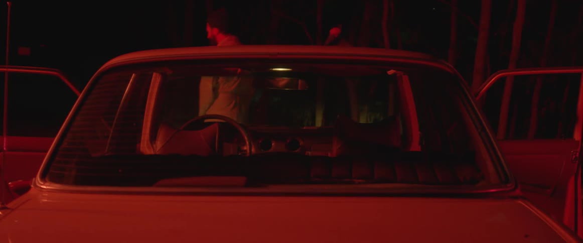 Two people dance behind a car at night
