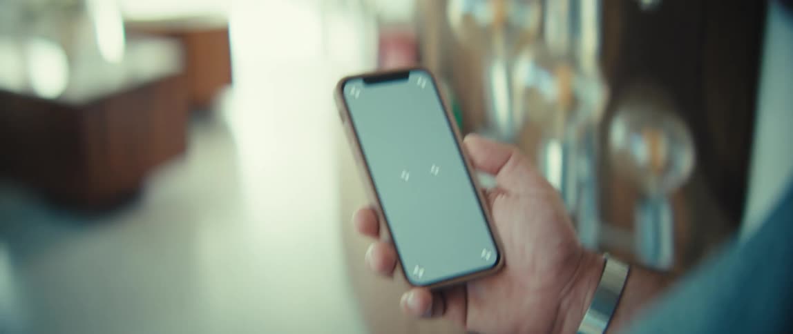 Hand holding smartphone with screen on in blurred indoor setting in the background