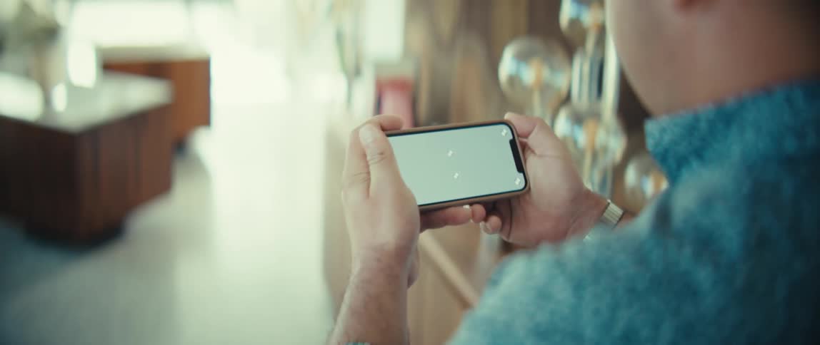 A person holds a smartphone horizontally with a green screen on the display interacting with the touch screen