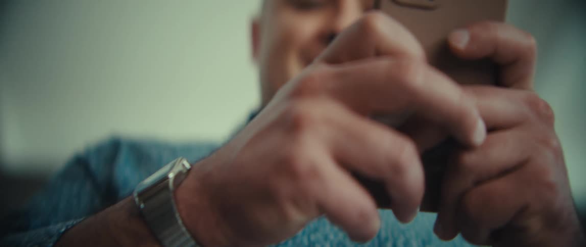 Man smiles as he walks in a room holding his phone with both hands as he texts