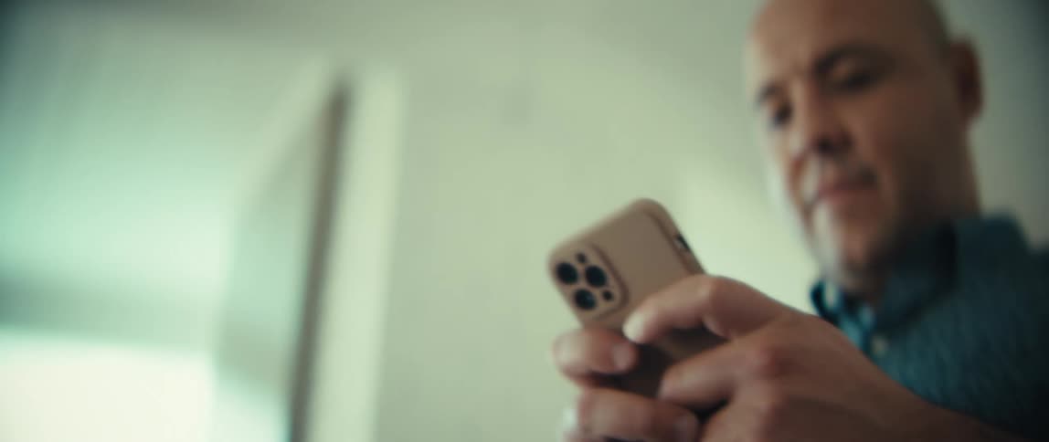 Man walks through a room holding his phone with both hands texting