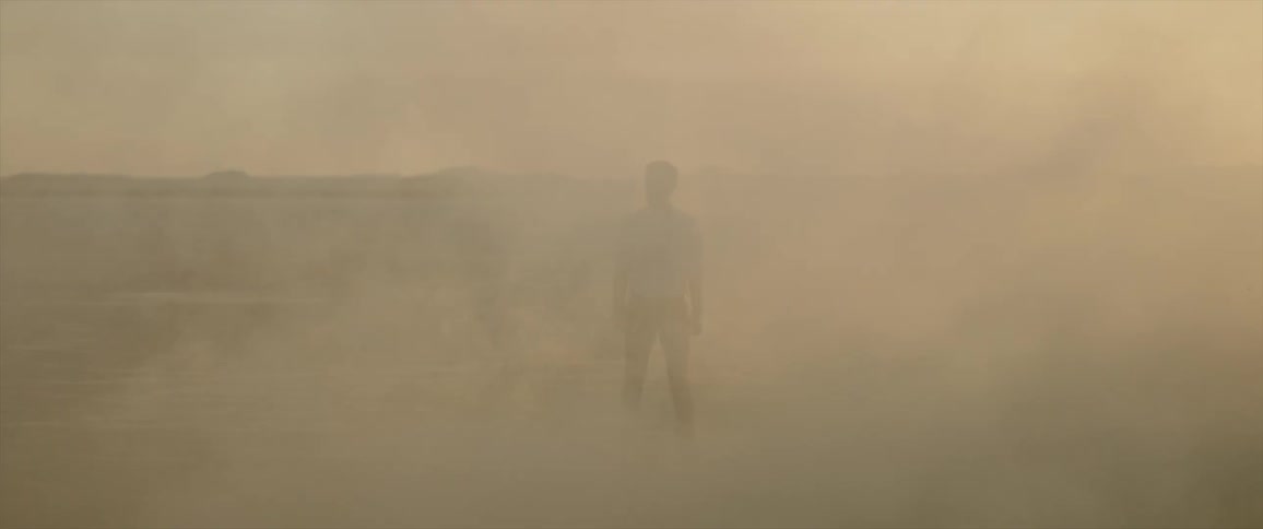 A man stands in the dust as a car speeds past