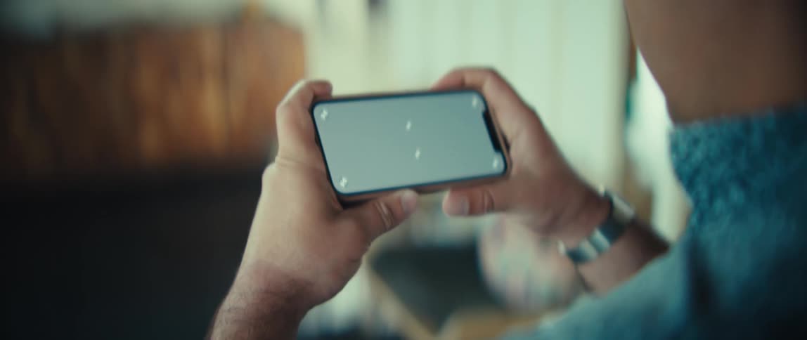 Man holds his phone sideways with both hands as he walks through a room