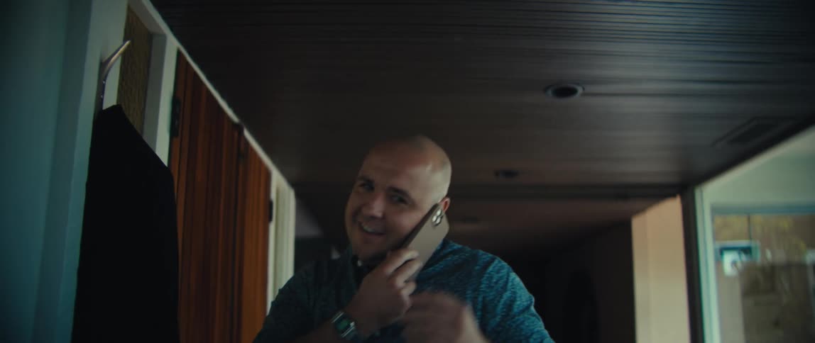 Man opens the door and walks into a house as he talks on his phone and hangs his jacket on the hook and cheers in celebration