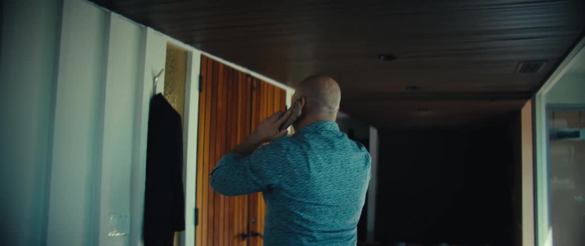 Man walks through a room talking on his phone as he raises his arms in celebration then takes his jacket and leaves